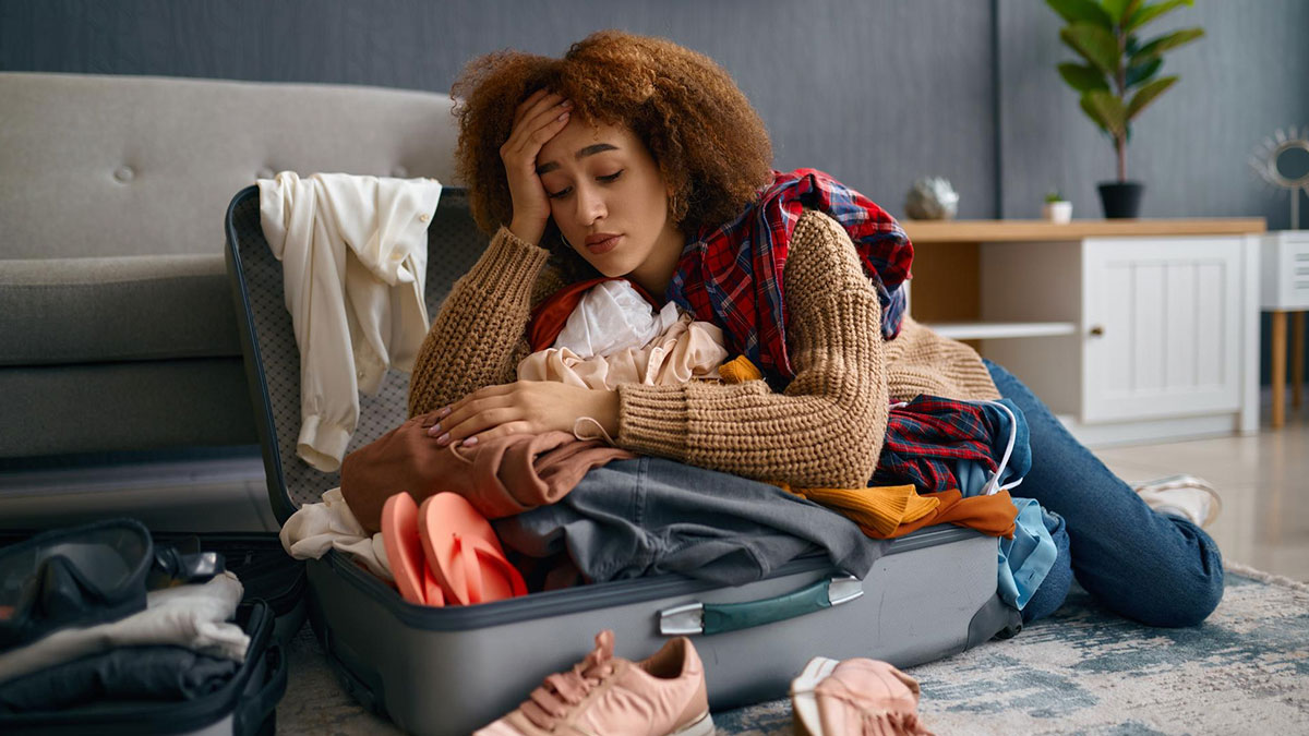Tired woman leaning on an open suitcase filled with clothes, reflecting stress about a homeless friend mooching off a couple.