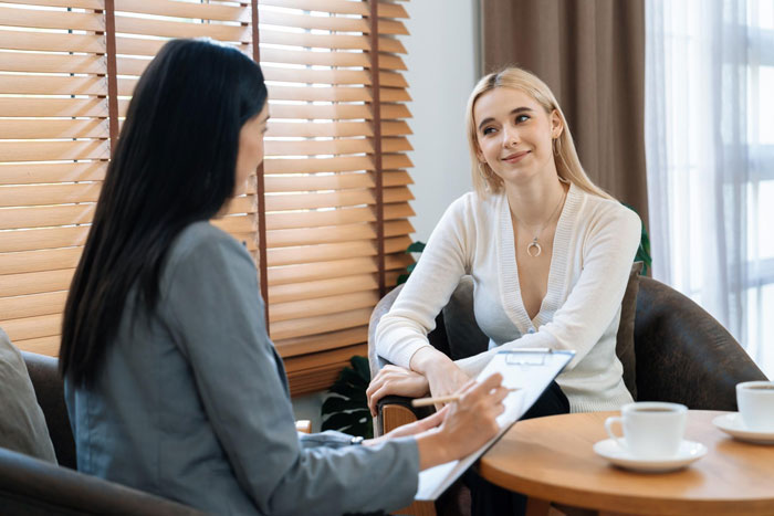 Two women having a serious conversation at a table, illustrating a homeless friend mooching off a couple scenario.