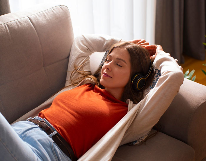 Young woman relaxing on a couch wearing headphones, representing a homeless friend mooching off a couple for months. Young woman relaxing on a couch wearing headphones, representing a homeless friend mooching off a couple for months.