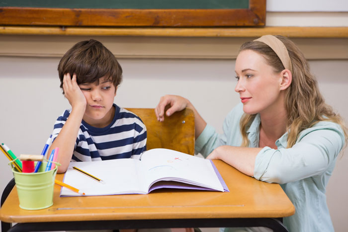 Sad 5-year-old boy left hungry at school sitting with a teacher after snack denied as consequence for fighting.
