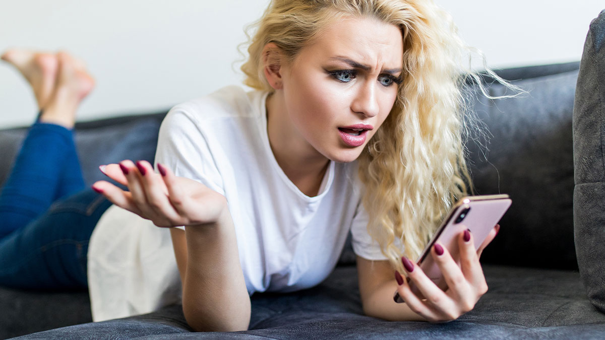Woman with blonde curly hair lying on sofa looking frustrated at phone, expressing tiredness in future stepkid situation