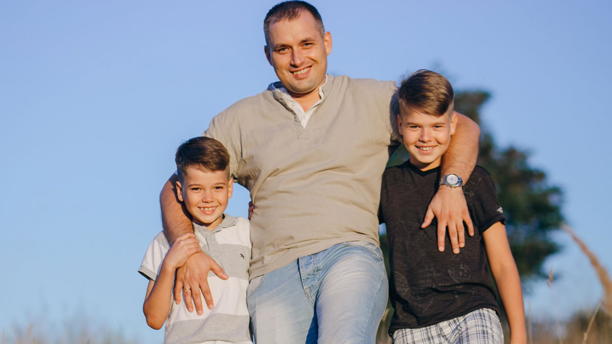 Father with two smiling sons outdoors, representing a rich dad taking his son on fancy trips.