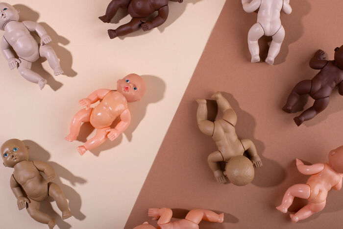 Various random baby dolls in diverse skin tones lying on beige and brown surfaces, representing childhood memories.