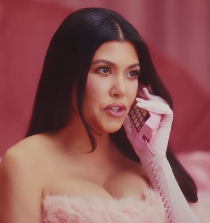 Kourtney Kardashian holding pink phone, promoting lollipops for women’s private parts, sparking reactions in a pink setting. Kourtney Kardashian holding pink phone, promoting lollipops for women’s private parts, sparking reactions in a pink setting.