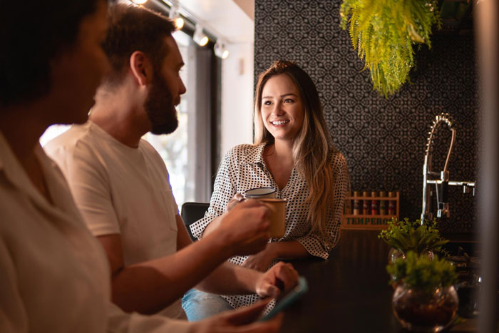 Woman nervously smiling while talking to an elite military diver in a cozy cafe, holding a coffee cup during their date. Woman nervously smiling while talking to an elite military diver in a cozy cafe, holding a coffee cup during their date.