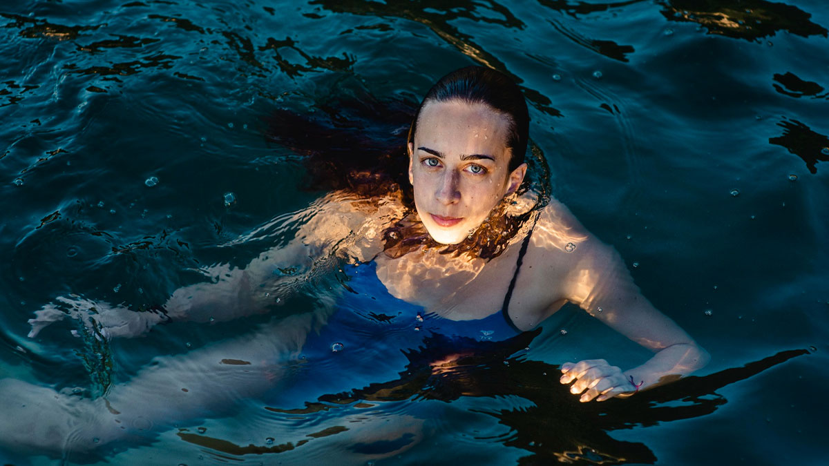 Woman swimming in deep water, possibly an elite military diver, with focused expression and wet hair slicked back.