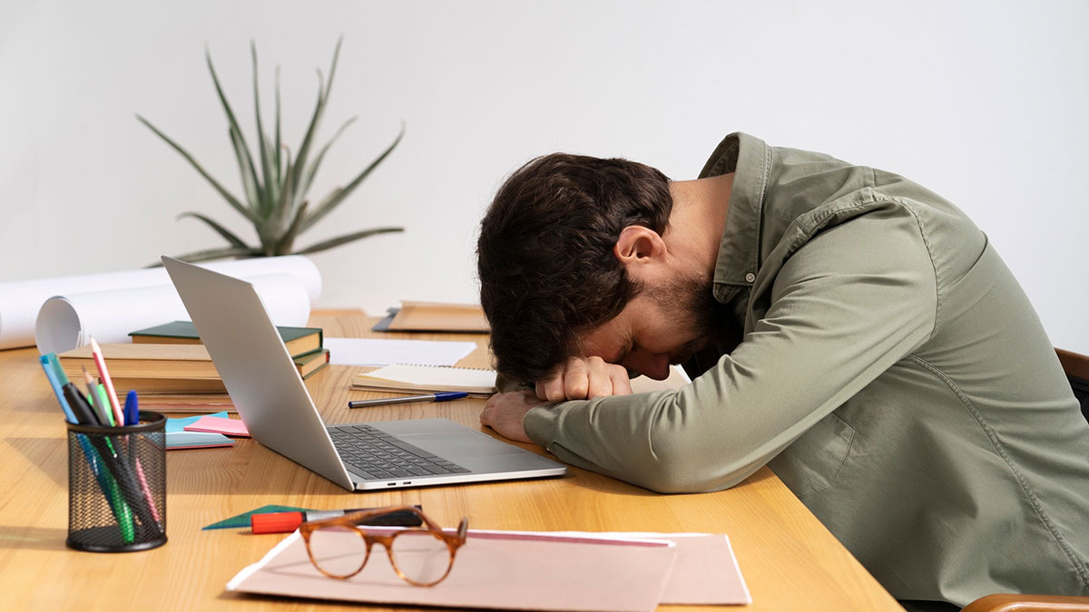 Man frustrated at desk with laptop and papers, illustrating life hacks that tricked people into extra work.