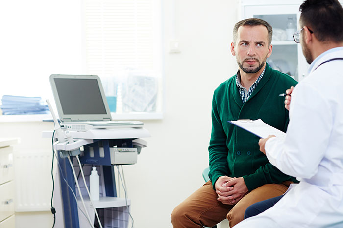 Man in green sweater consulting with doctor during a medical appointment in a bright clinic room.