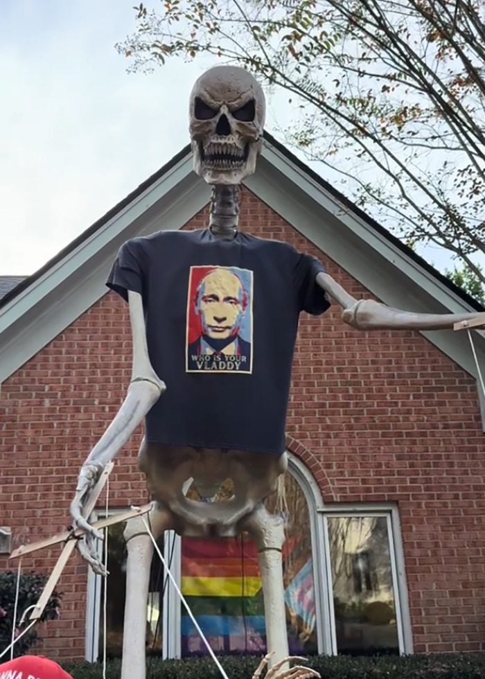 Skeleton Halloween display wearing a political shirt in an elaborate anti-MAGA decoration with colorful flags outside a brick house. Skeleton Halloween display wearing a political shirt in an elaborate anti-MAGA decoration with colorful flags outside a brick house.