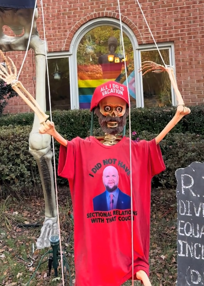 Skeleton figure in an anti-MAGA Halloween display wearing a red hat and shirt with a humorous political message. Skeleton figure in an anti-MAGA Halloween display wearing a red hat and shirt with a humorous political message.