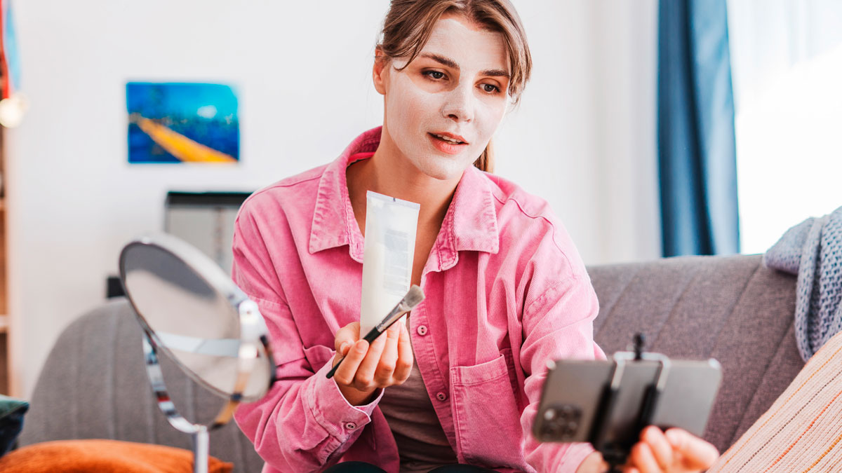 Gym influencer applying face mask and recording skincare routine with smartphone in a cozy home setting.