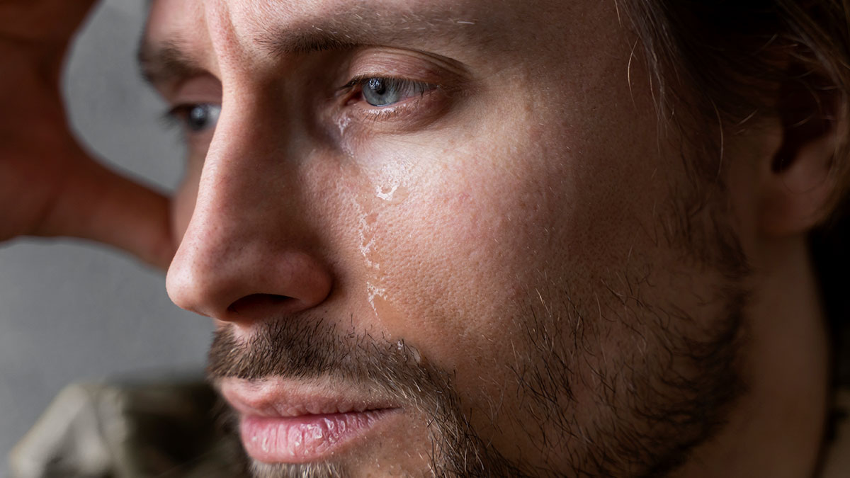 Close-up of a man with a tear on his cheek, reflecting pain as he learns about fiancu00e9e's love for her friend.