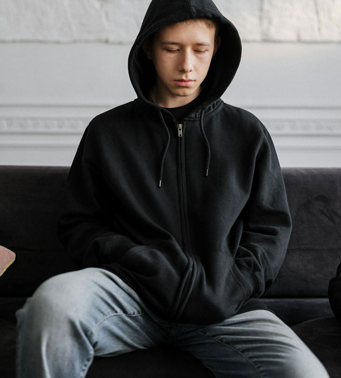Teenage son in black hoodie sitting with a downcast expression, reflecting parents spoiling daughter and neglecting him. Teenage son in black hoodie sitting with a downcast expression, reflecting parents spoiling daughter and neglecting him.