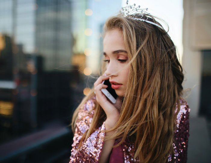 Young woman wearing a tiara and sequin jacket, talking on phone, illustrating parents spoiling daughter and financial struggle. Young woman wearing a tiara and sequin jacket, talking on phone, illustrating parents spoiling daughter and financial struggle.