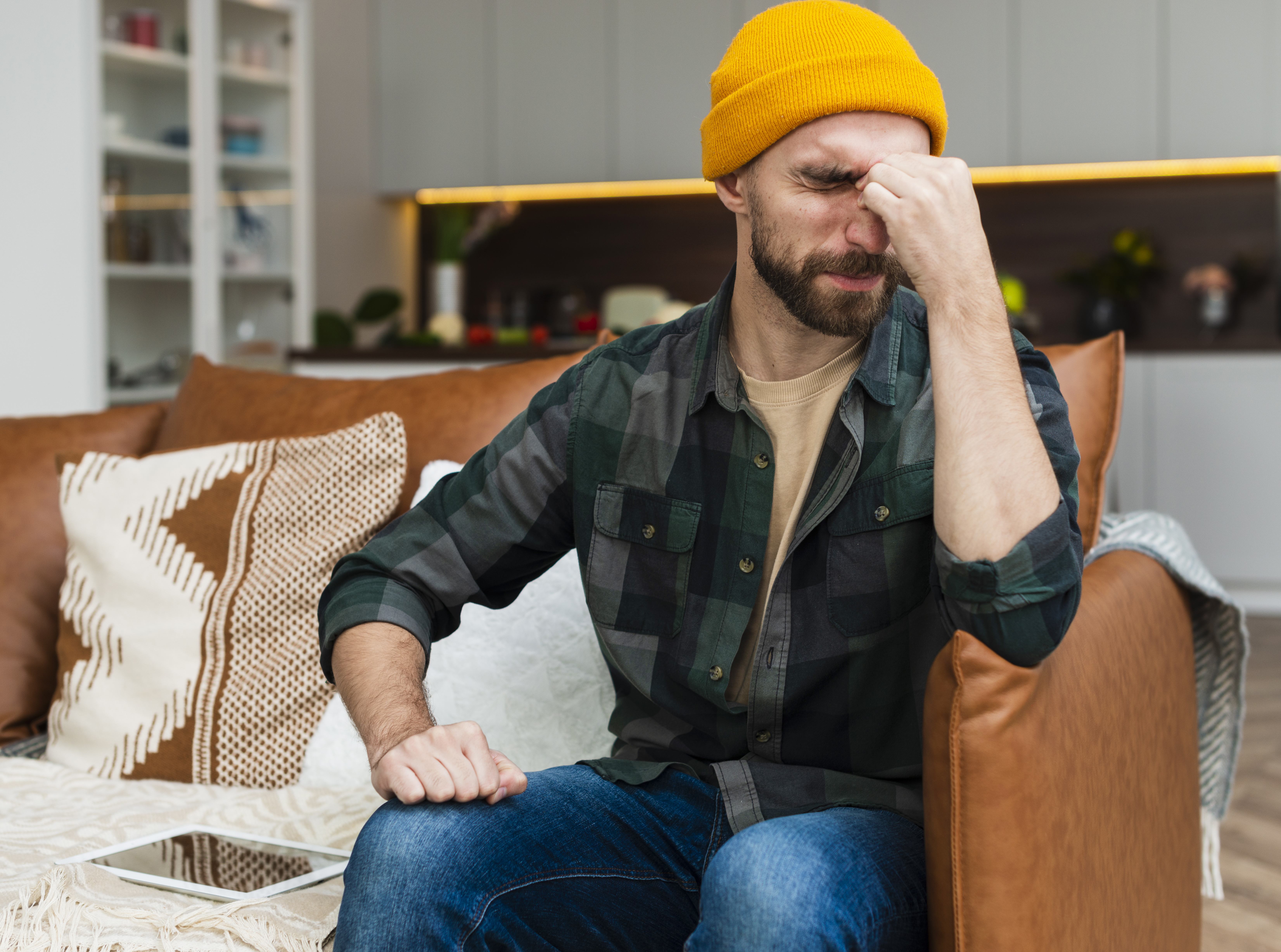 Man in yellow beanie sitting on couch looking stressed, representing issues with combined income and money selfishness. Man in yellow beanie sitting on couch looking stressed, representing issues with combined income and money selfishness.