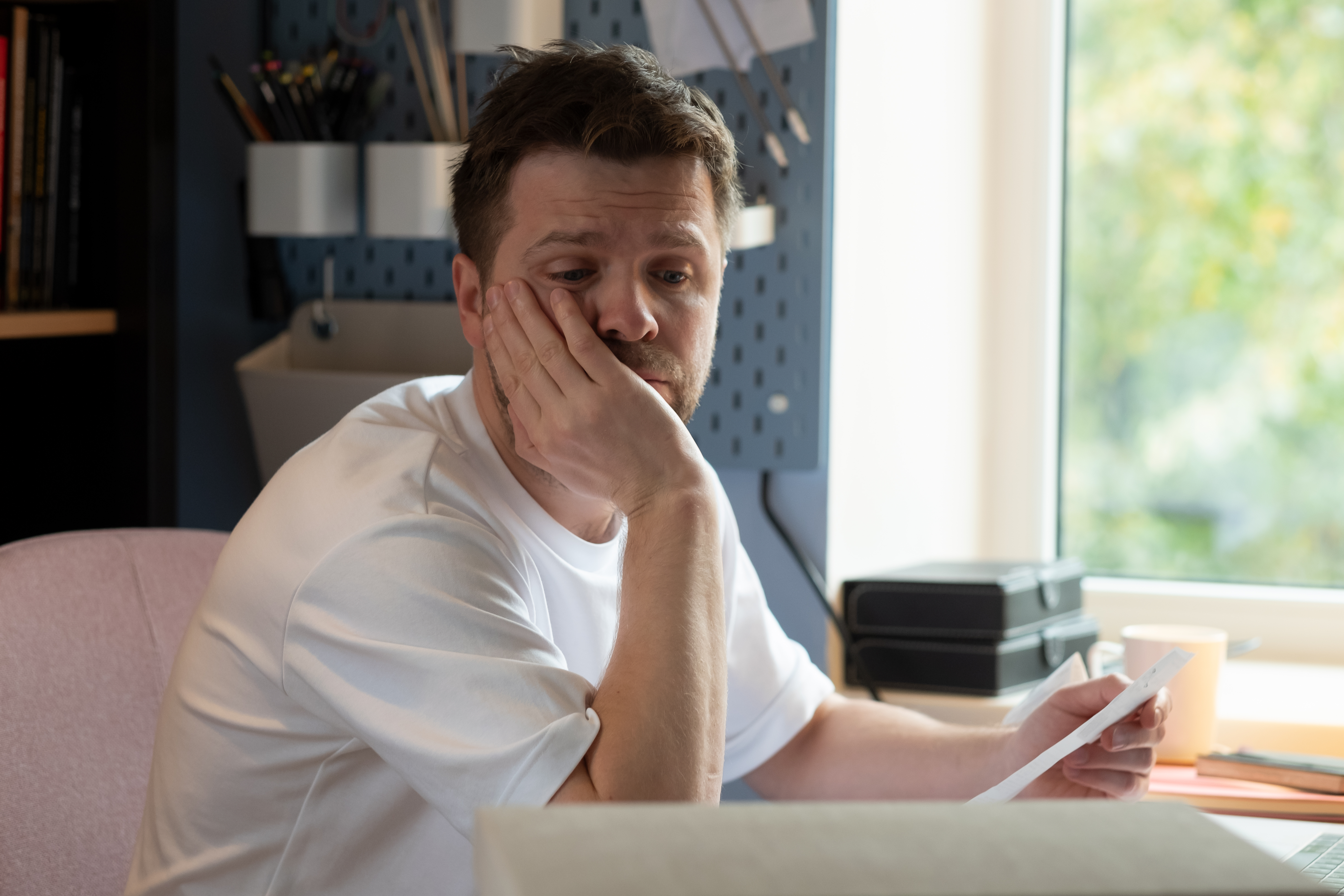 Man looking worried at a letter with hand on face, reflecting on woman going to gala with client as date situation. Man looking worried at a letter with hand on face, reflecting on woman going to gala with client as date situation.