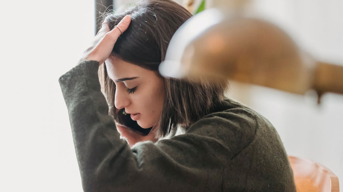 Woman on phone looking stressed, holding her head, illustrating a tense call about daughtersu2019 lunch plans.