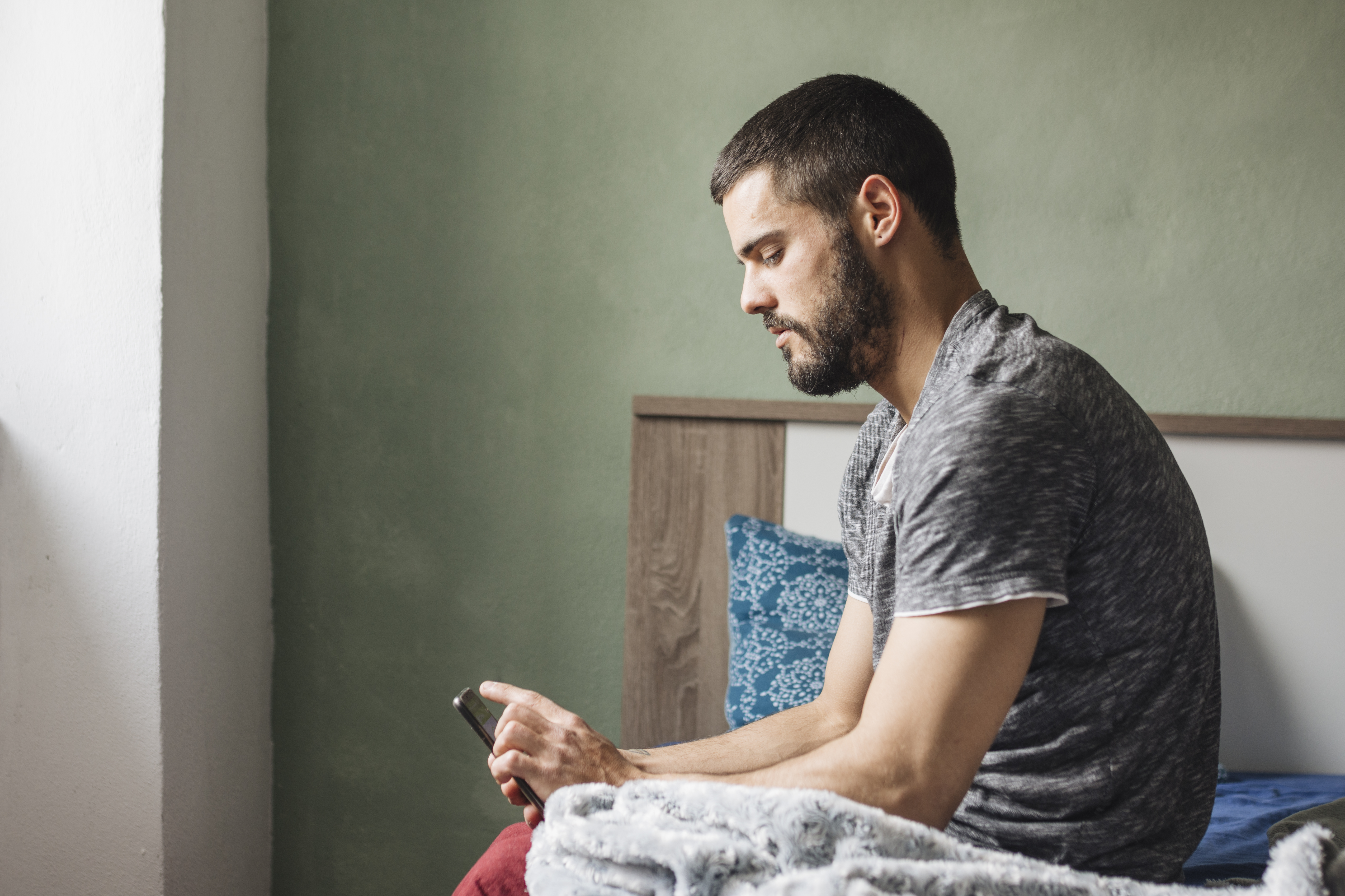Man sitting on bed looking at phone, reflecting, symbolizing husband questioning everything after woman goes to gala with client. Man sitting on bed looking at phone, reflecting, symbolizing husband questioning everything after woman goes to gala with client.