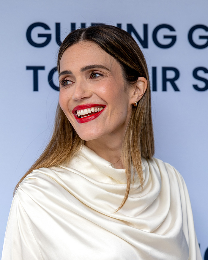 Mandy Moore smiling with red lipstick and sleek hair in a white satin outfit, showing her new unrecognizable look. Mandy Moore smiling with red lipstick and sleek hair in a white satin outfit, showing her new unrecognizable look.