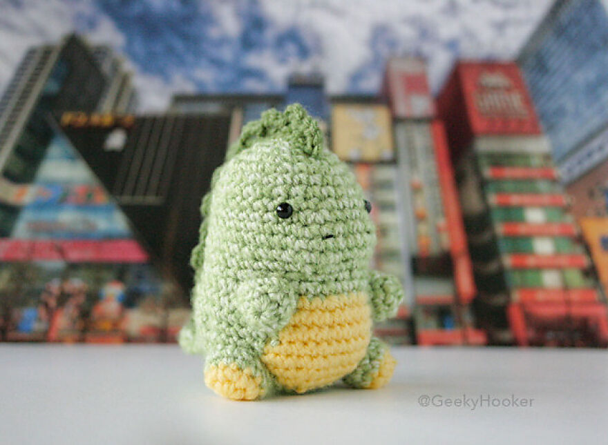 Crochet animal with personality, featuring a small green and yellow dinosaur amigurumi against a cityscape background.