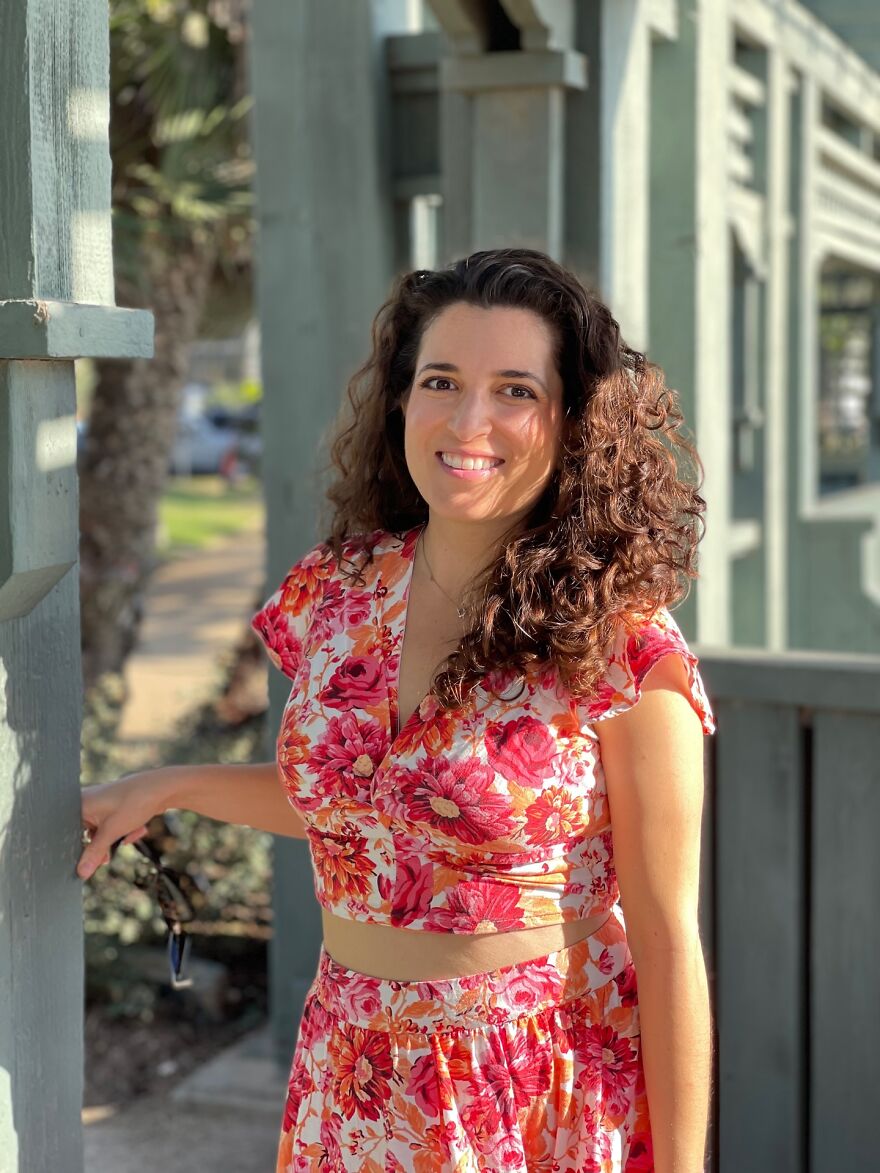 Woman with curly hair and floral outfit smiling outdoors, featured in billboard campaign to find love. Woman with curly hair and floral outfit smiling outdoors, featured in billboard campaign to find love.
