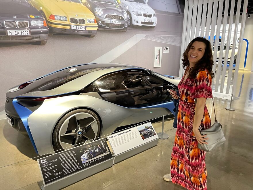 Woman smiling and standing near a futuristic car in a museum, related to billboard campaign to find love responses. Woman smiling and standing near a futuristic car in a museum, related to billboard campaign to find love responses.