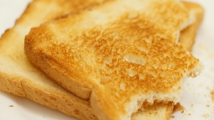 Two slices of toasted bread on a white plate with one slice partially eaten, showing golden brown texture.