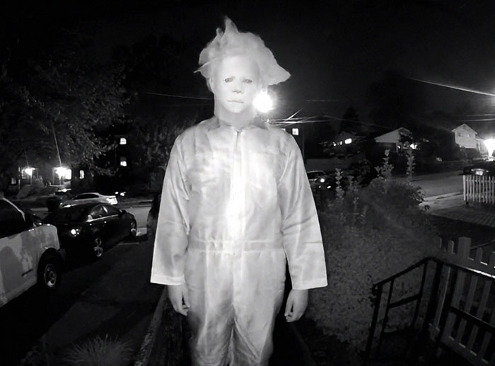 Person wearing a disturbing mask and costume stands on a porch during a doorbell prank at night. Person wearing a disturbing mask and costume stands on a porch during a doorbell prank at night.
