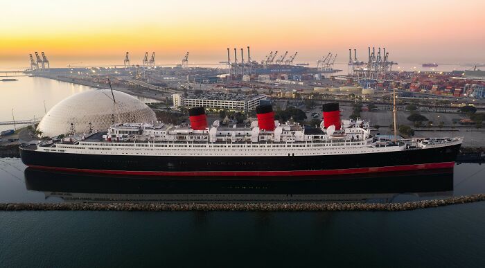 Historic ocean liner docked at port during sunset, a spooky destination for haunting Halloween visits.
