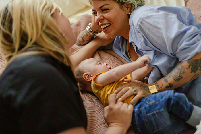 A couple lies on a bed smiling at their baby, highlighting IVF and family bonding moments. A couple lies on a bed smiling at their baby, highlighting IVF and family bonding moments.