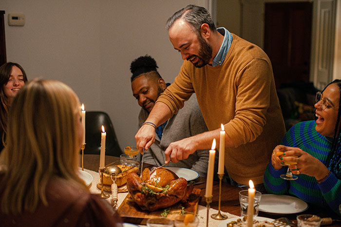 Man carving turkey at Thanksgiving dinner while family shares a tense moment over relationship conflict.