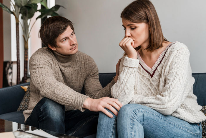 A distressed woman and her husband sitting on a couch during a tense discussion about rude MIL behavior. A distressed woman and her husband sitting on a couch during a tense discussion about rude MIL behavior.