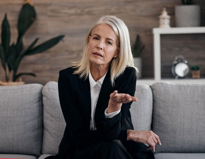 Middle-aged woman in business attire sitting on a couch looking frustrated reflecting rude MIL behavior and family conflict. Middle-aged woman in business attire sitting on a couch looking frustrated reflecting rude MIL behavior and family conflict.