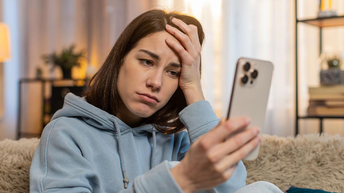 Young woman looking frustrated and upset while holding a smartphone, dealing with nonstop calls from her MIL.