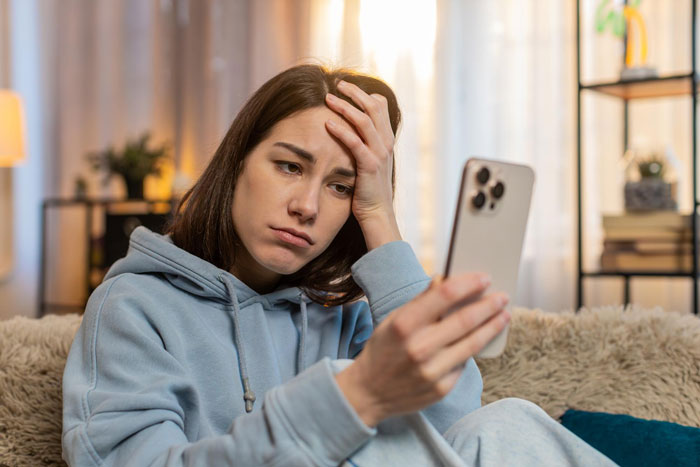 Young woman in a hoodie looking frustrated at her smartphone, reacting to nonstop mystery calls from her MIL. Young woman in a hoodie looking frustrated at her smartphone, reacting to nonstop mystery calls from her MIL.