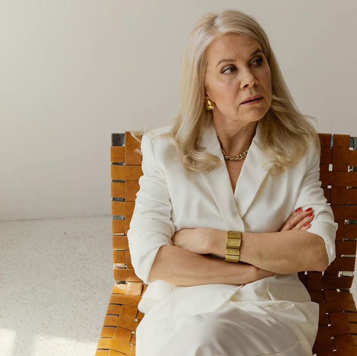 Middle-aged woman in white outfit sitting with crossed arms, appearing upset during wedding attention conflict. Middle-aged woman in white outfit sitting with crossed arms, appearing upset during wedding attention conflict.