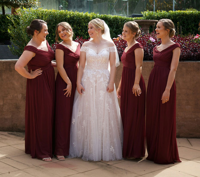 Bride in white wedding dress surrounded by bridesmaids in burgundy gowns during a wedding with MIL attention drama. Bride in white wedding dress surrounded by bridesmaids in burgundy gowns during a wedding with MIL attention drama.