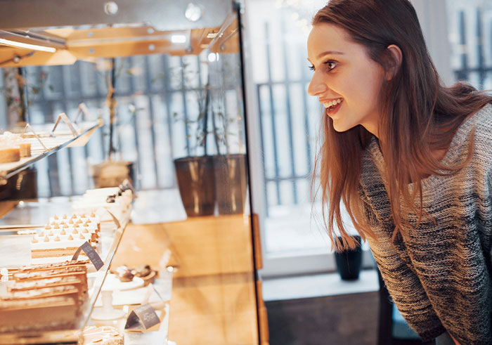 Young woman smiling and leaning forward to look at pastries in a bakery, capturing a moment of social cues misreading.