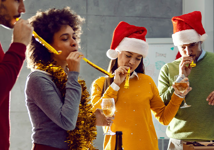 Group of young adults in festive hats drinking wine and blowing party horns, capturing a social cues misread moment.