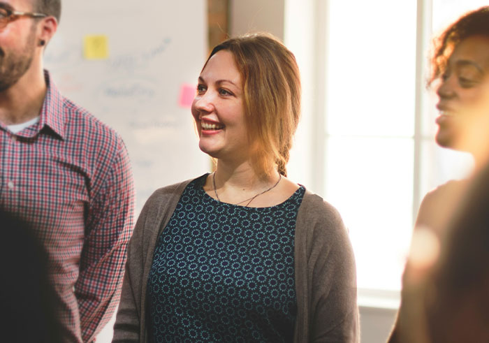 Group of people socializing indoors, focusing on a smiling woman in casual attire experiencing social cue misread moments.