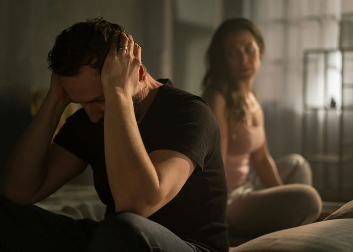 Man holding head in distress while woman sits in background, reflecting tension after failed reconciliation attempt.