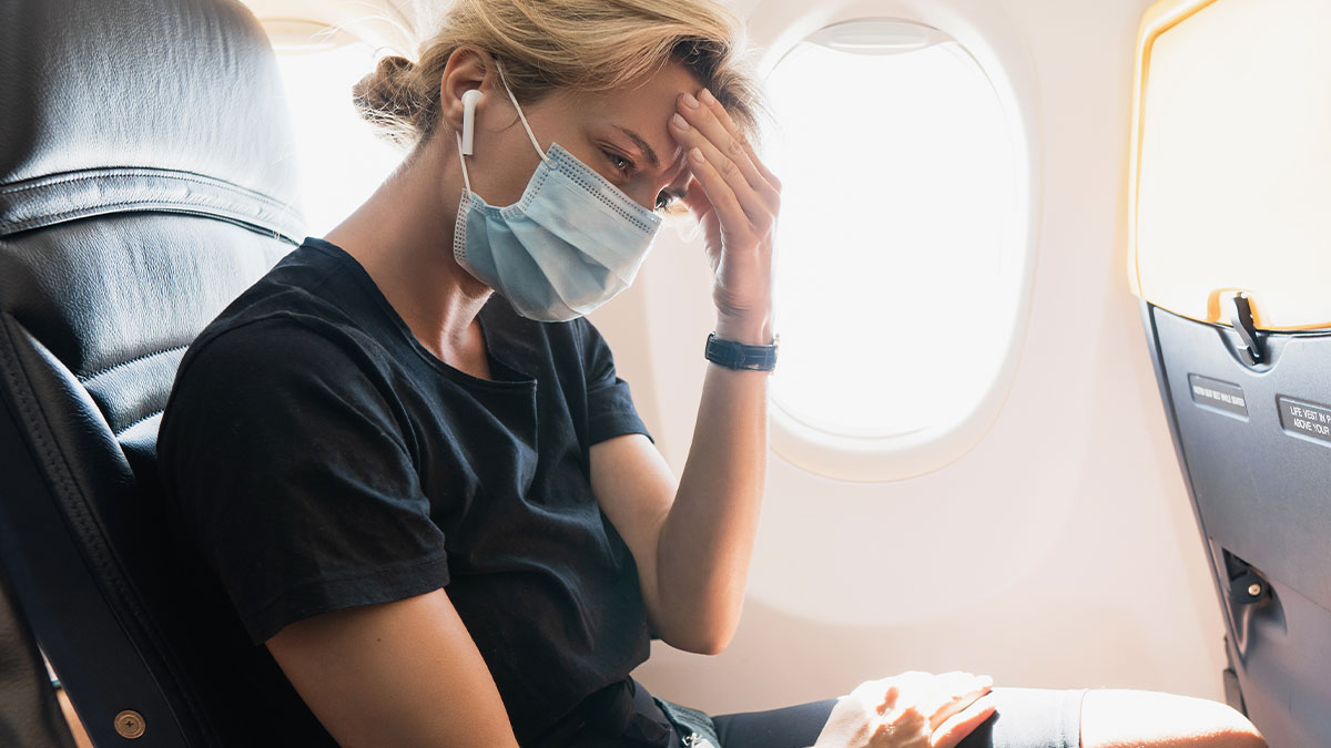Passenger on airplane looking stressed while wearing a mask, depicting frustration during toddler meltdown on a flight.