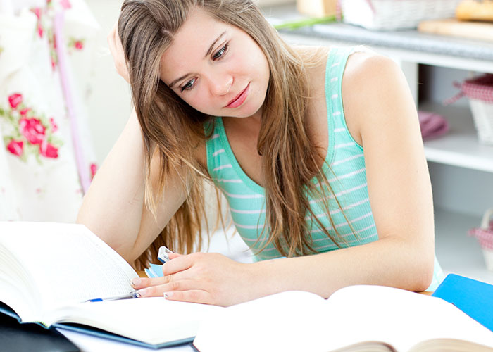 Young woman studying alone at home, showing a thoughtful expression while reading and taking notes during quiet time. Young woman studying alone at home, showing a thoughtful expression while reading and taking notes during quiet time.