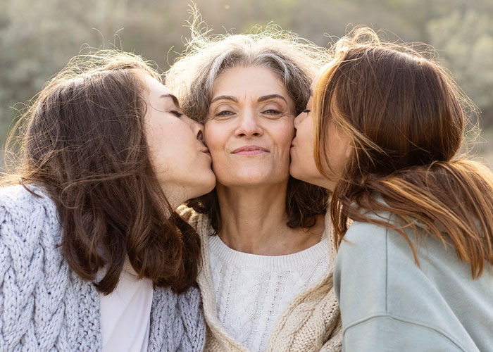Mom with two daughters outdoors, showing affection with kisses, highlighting mom admits she likes one daughter more than the other. Mom with two daughters outdoors, showing affection with kisses, highlighting mom admits she likes one daughter more than the other.