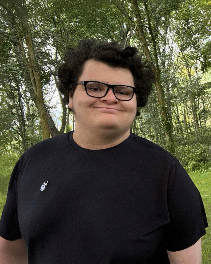 Teen boy wearing glasses and black shirt, standing outdoors with trees in the background, related to haunting 911 call case.