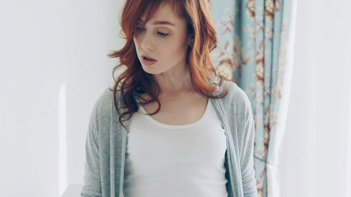 Red-haired woman in casual clothing looking down thoughtfully, representing horrifyingly cruel person concept.