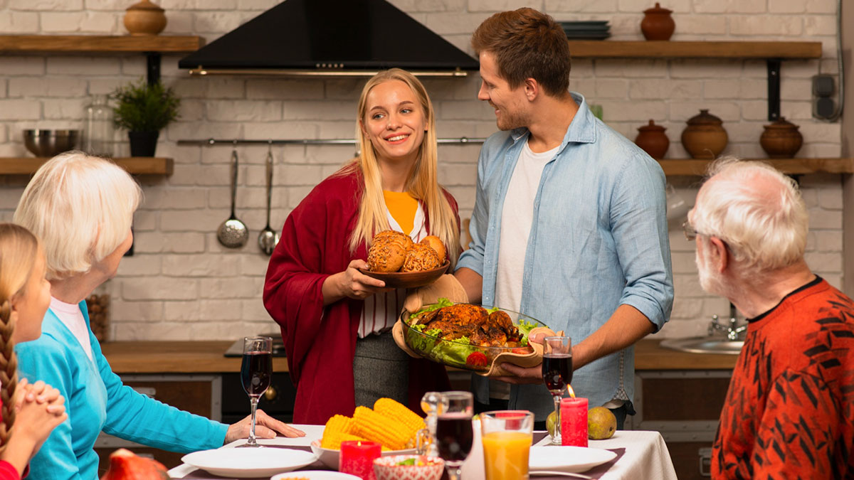 A young couple serving food to family at dinner, illustrating relationships impacted by gender roles and unfair expectations.