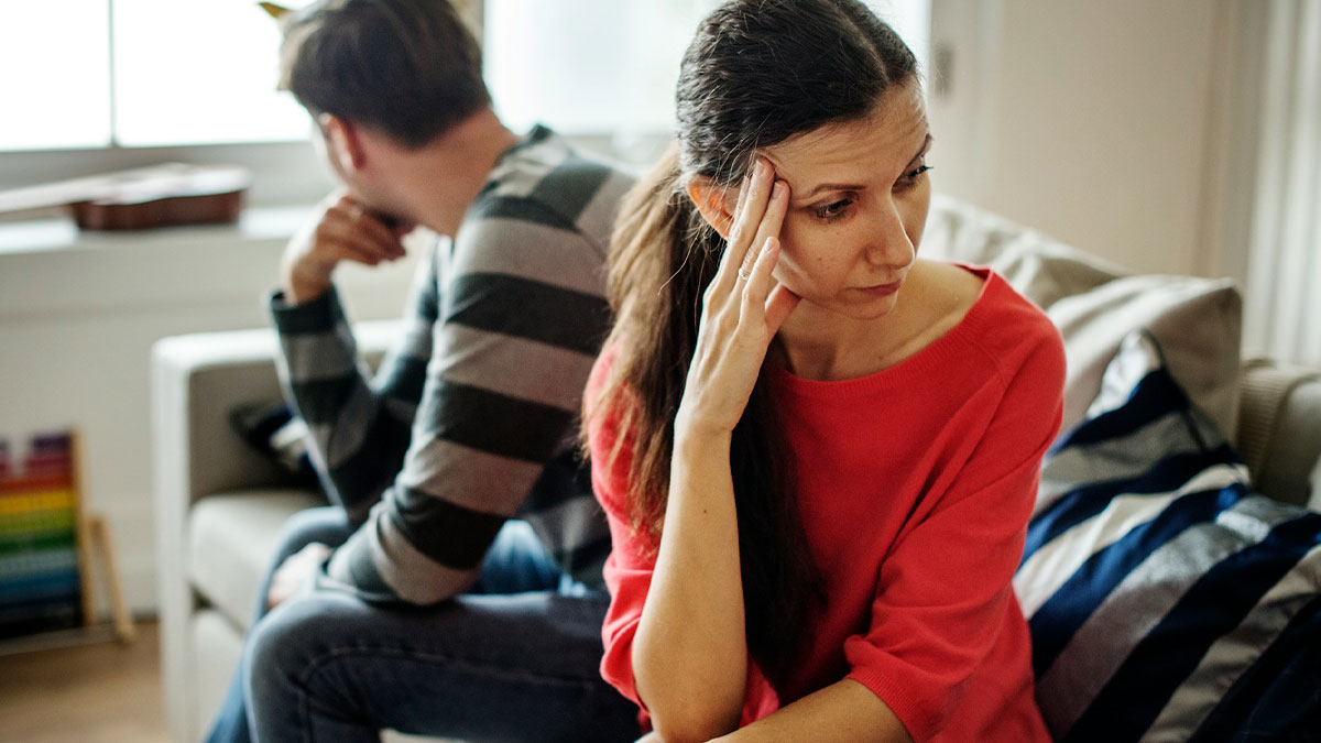 Couple sitting apart on a couch, looking upset and distant, illustrating challenges in relationship advice.