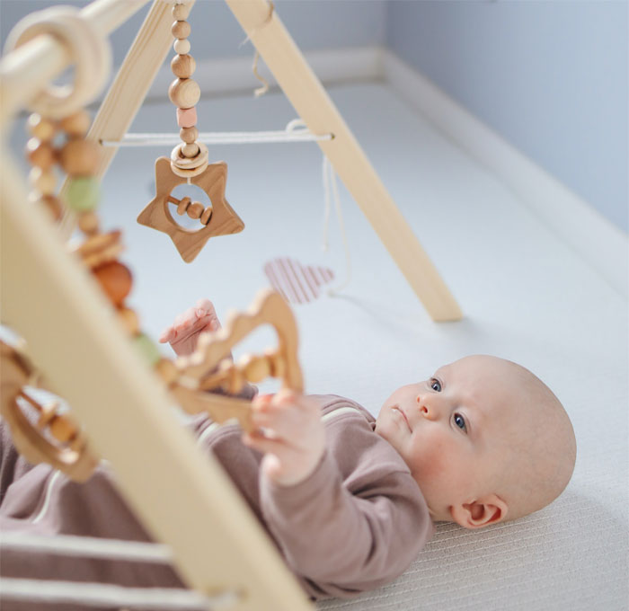 Baby lying under wooden play gym, focused on hanging toys in a calm nursery setting. Baby lying under wooden play gym, focused on hanging toys in a calm nursery setting.