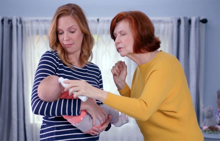 Woman holding her baby and gently stopping mother-in-law from kissing the newborn in a home setting. Woman holding her baby and gently stopping mother-in-law from kissing the newborn in a home setting.